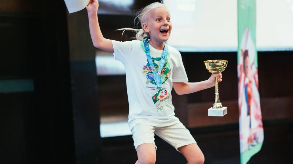 Eduard Florin Ștefan idicând un trofeu de aur și o diplomă la o festivitate de premiere, purtând o medalie la gât