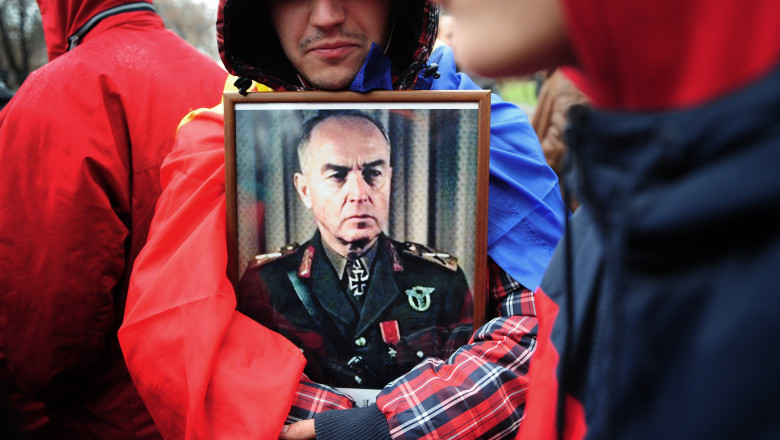 Participant la un eveniment public ținând în brațe un portret înrămat al unui lider militar din perioada celui de-al Doilea Război Mondial.