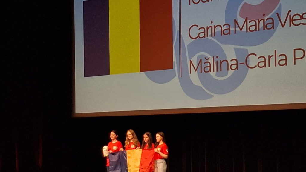 Eleve din România pe podium, ținând steagul României, în cadrul unei ceremonii pe scenă
