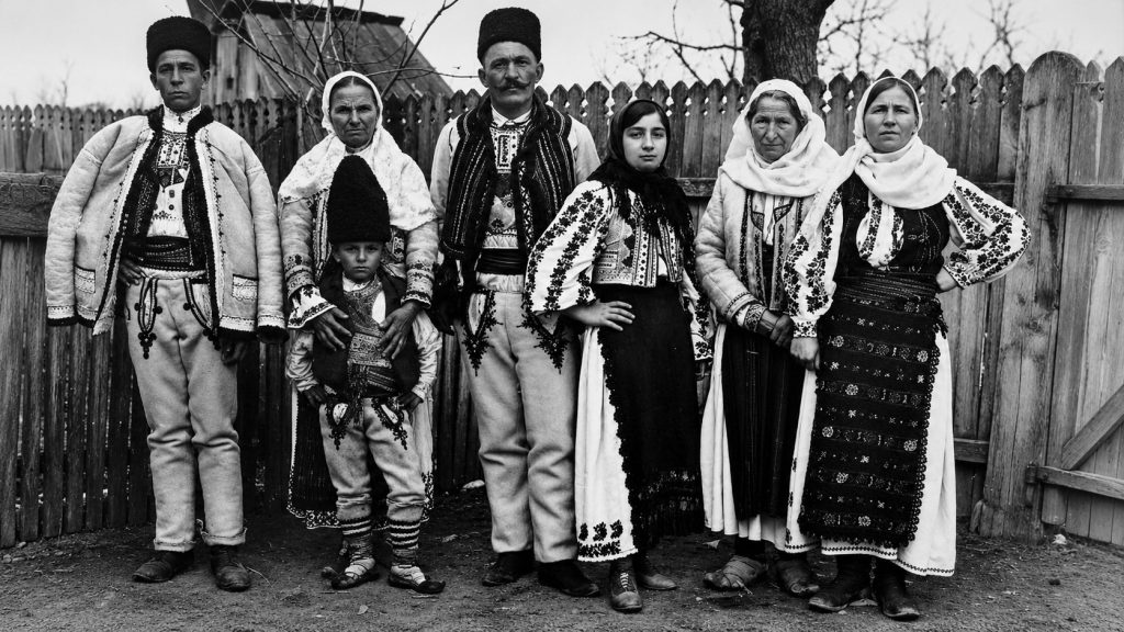 Familie din România îmbrăcată în costume populare tradiționale, fotografie istorică alb-negru în mediul rural